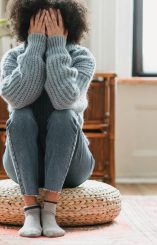 Woman sitting on cushion with face in hands, overwhelmed by invisible grief.