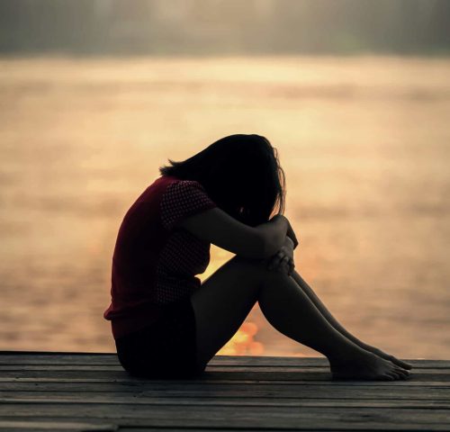 A grieving woman sitting alone at sunset, reflecting the weight and stillness of loss.