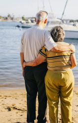 Older couple embracing by the water, symbolizing enduring love and companionship through grief.